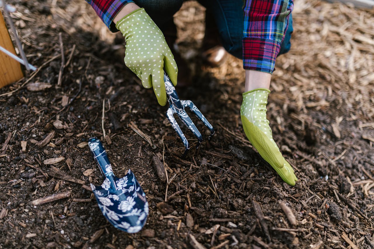 services-03 A person wearing gloves using garden tools in soil for planting.
